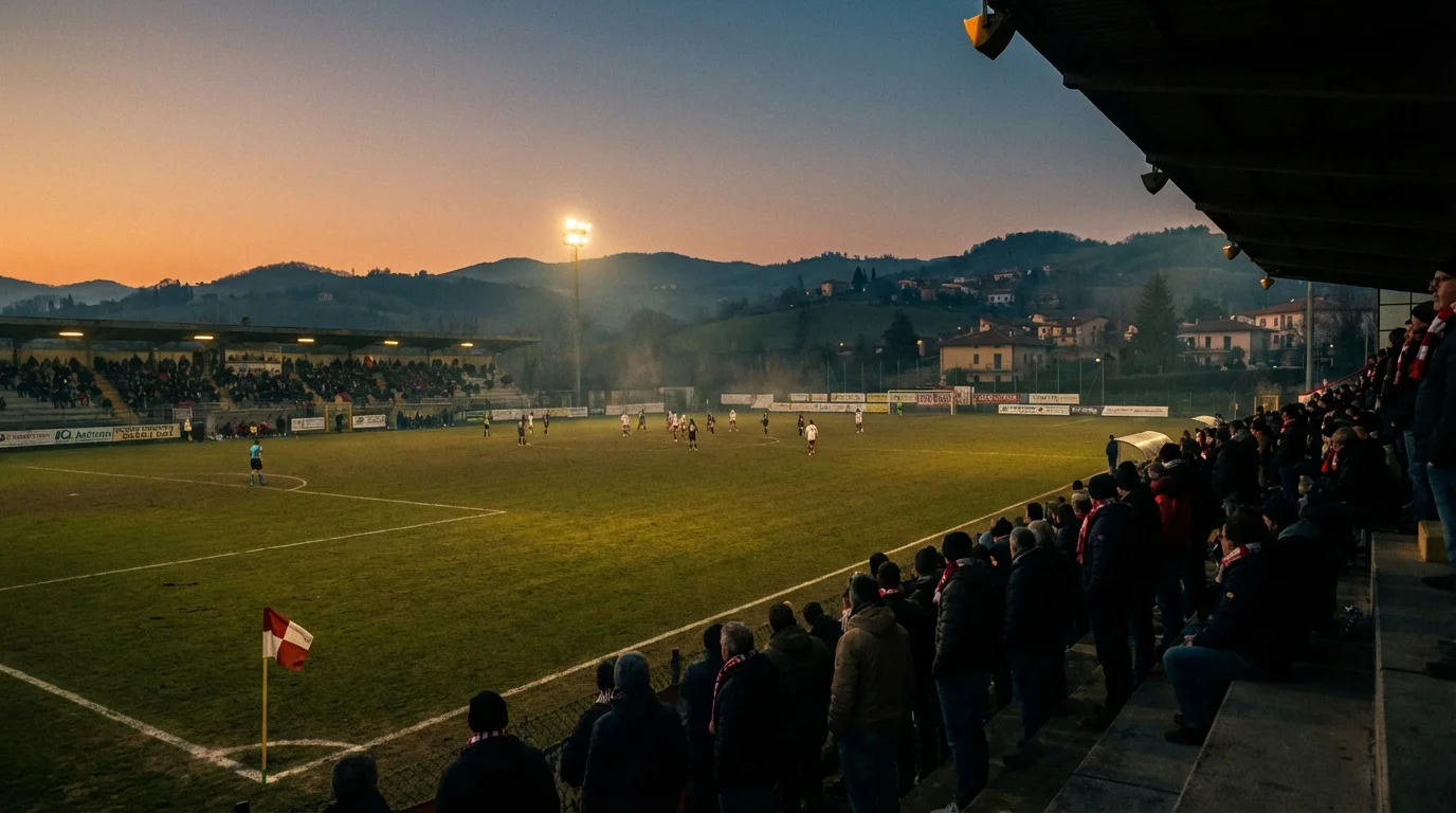 Piccolo stadio di provincia illuminato per una partita serale dei turni preliminari di Coppa Italia